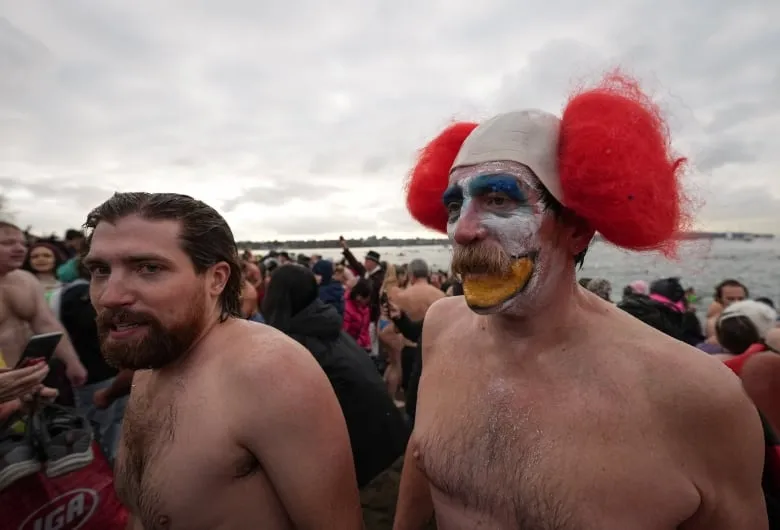 A man with clown makeup and others return to the shore after taking a dip in ocean water on New Year's Day.